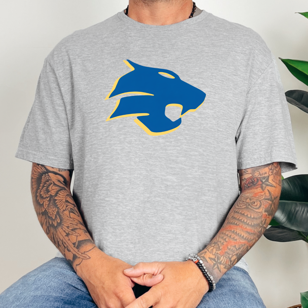 Person wearing a gray t-shirt with a blue and yellow graphic design, sitting against a neutral background.