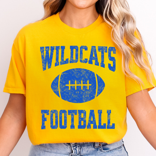 A woman wearing a  gold colored t-shirt with a blue distressed graphic that reads 'WILDCATS FOOTBALL' with a football in the center.
