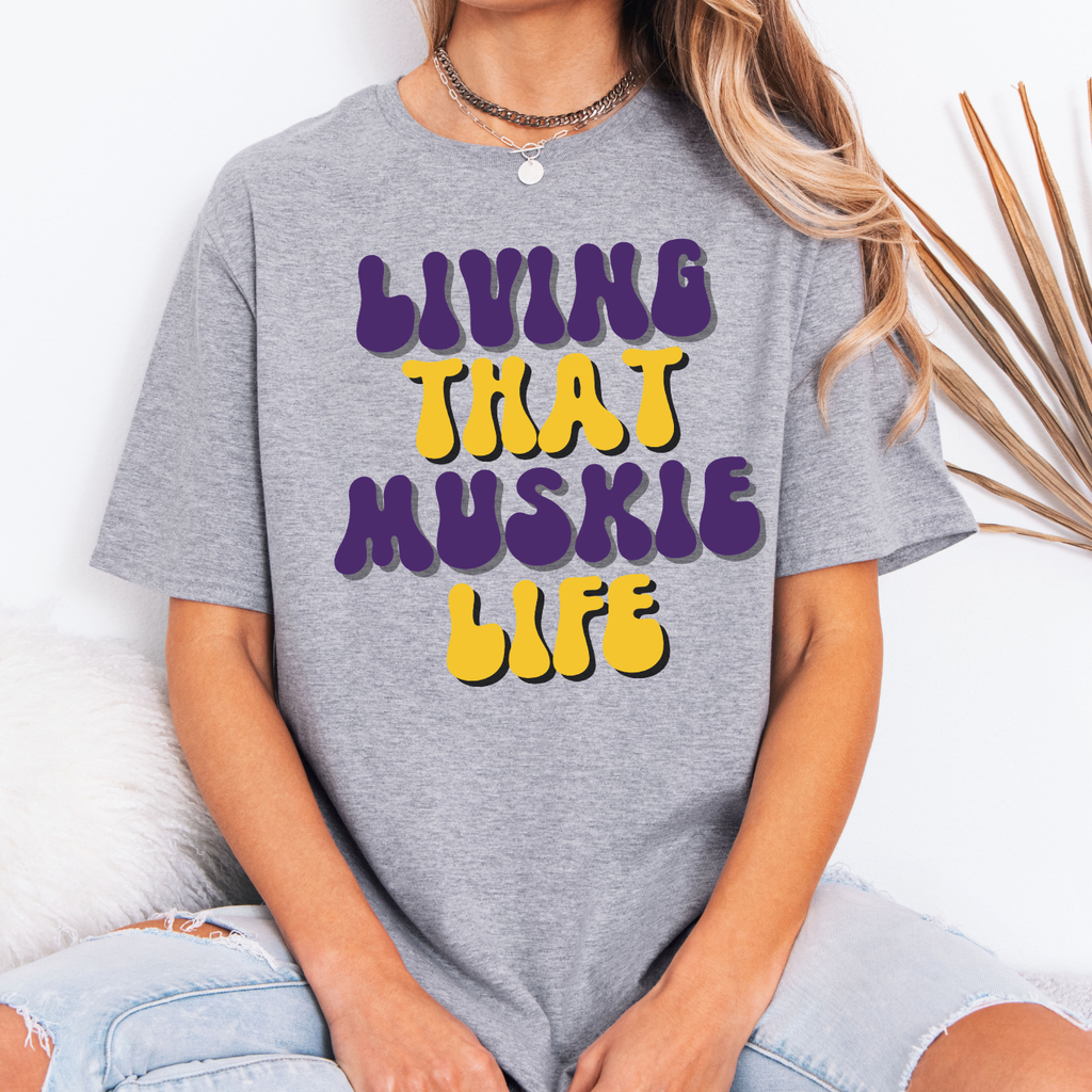 Person wearing a gray t-shirt with colorful text 'LIVING THAT MUSKIE LIFE' on a white background