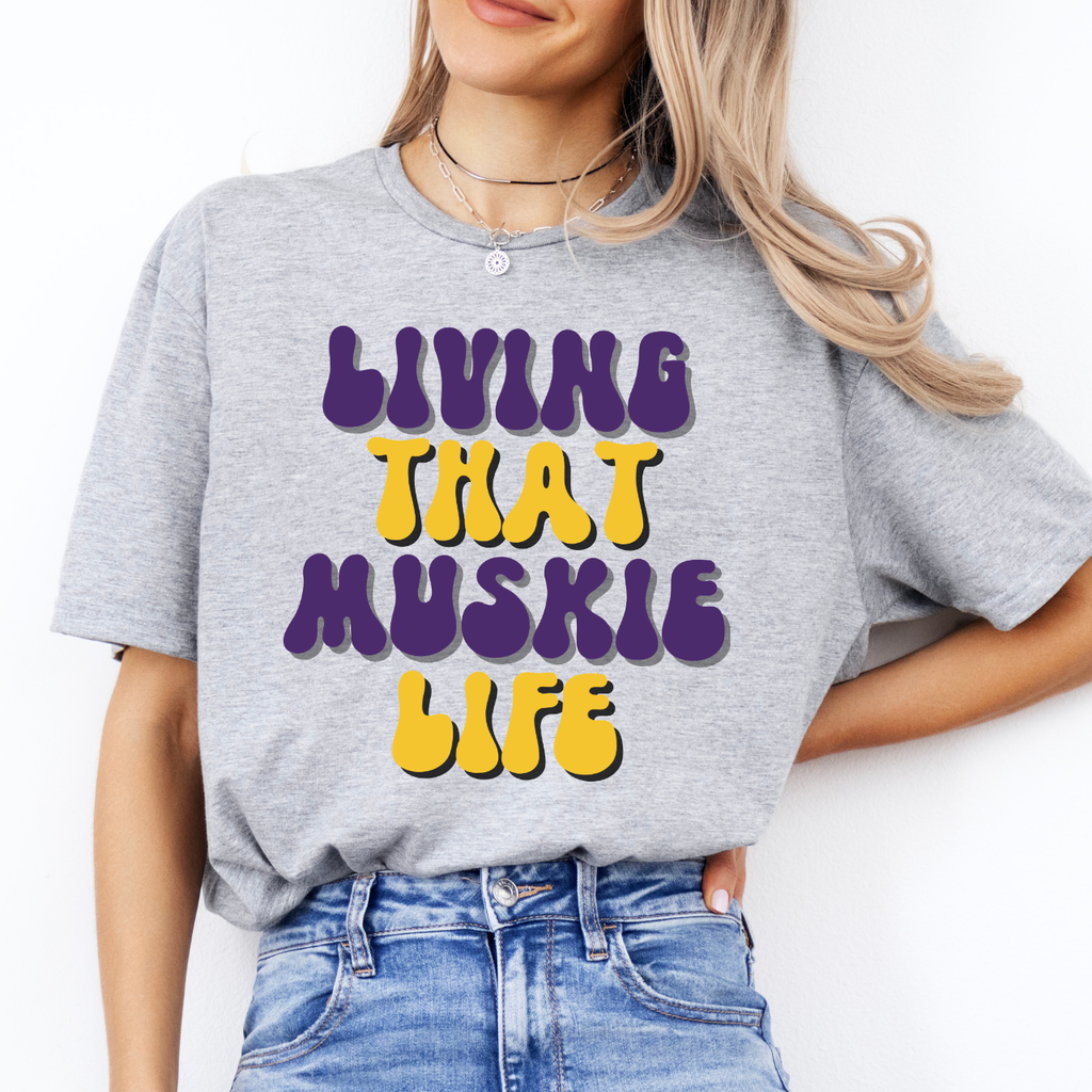 Person wearing a gray t-shirt with colorful text 'LIVING THAT MUSKIE LIFE' on a white background