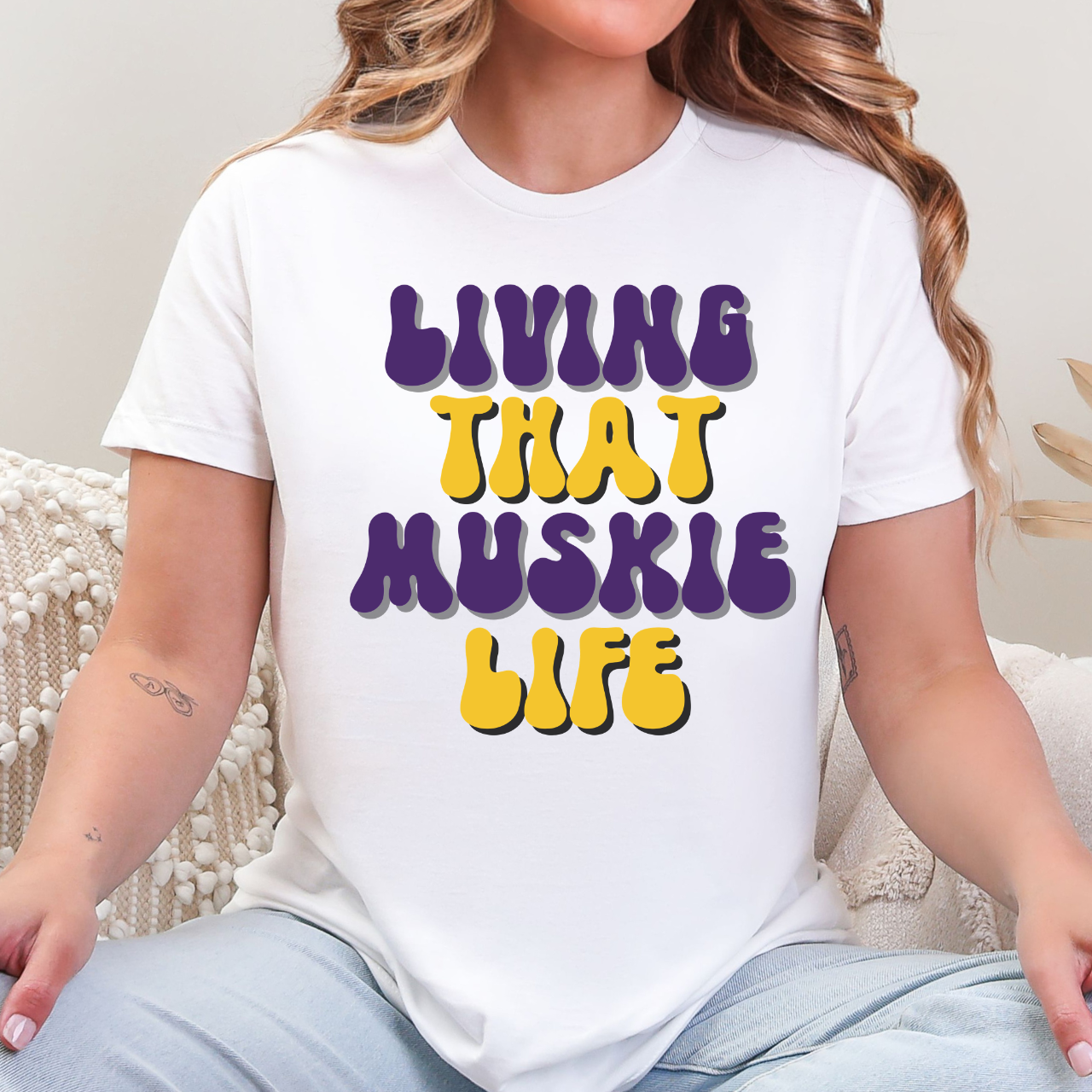 Person wearing a white t-shirt with 'LIVING THAT MUSKIE LIFE' text in purple and yellow.