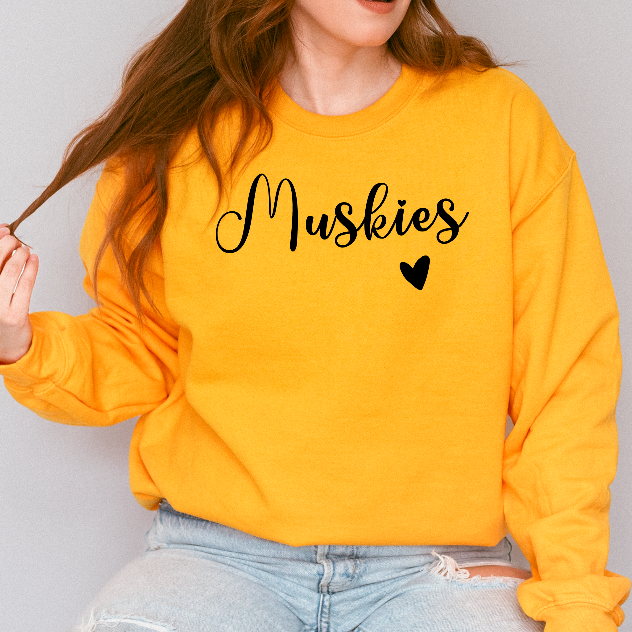 Person wearing a yellow sweatshirt with 'Muskies' text and heart symbol on a plain background