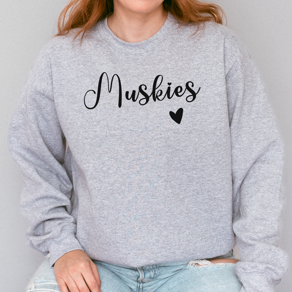Person wearing a gray sweatshirt with 'Muskies' and a heart graphic on a plain background