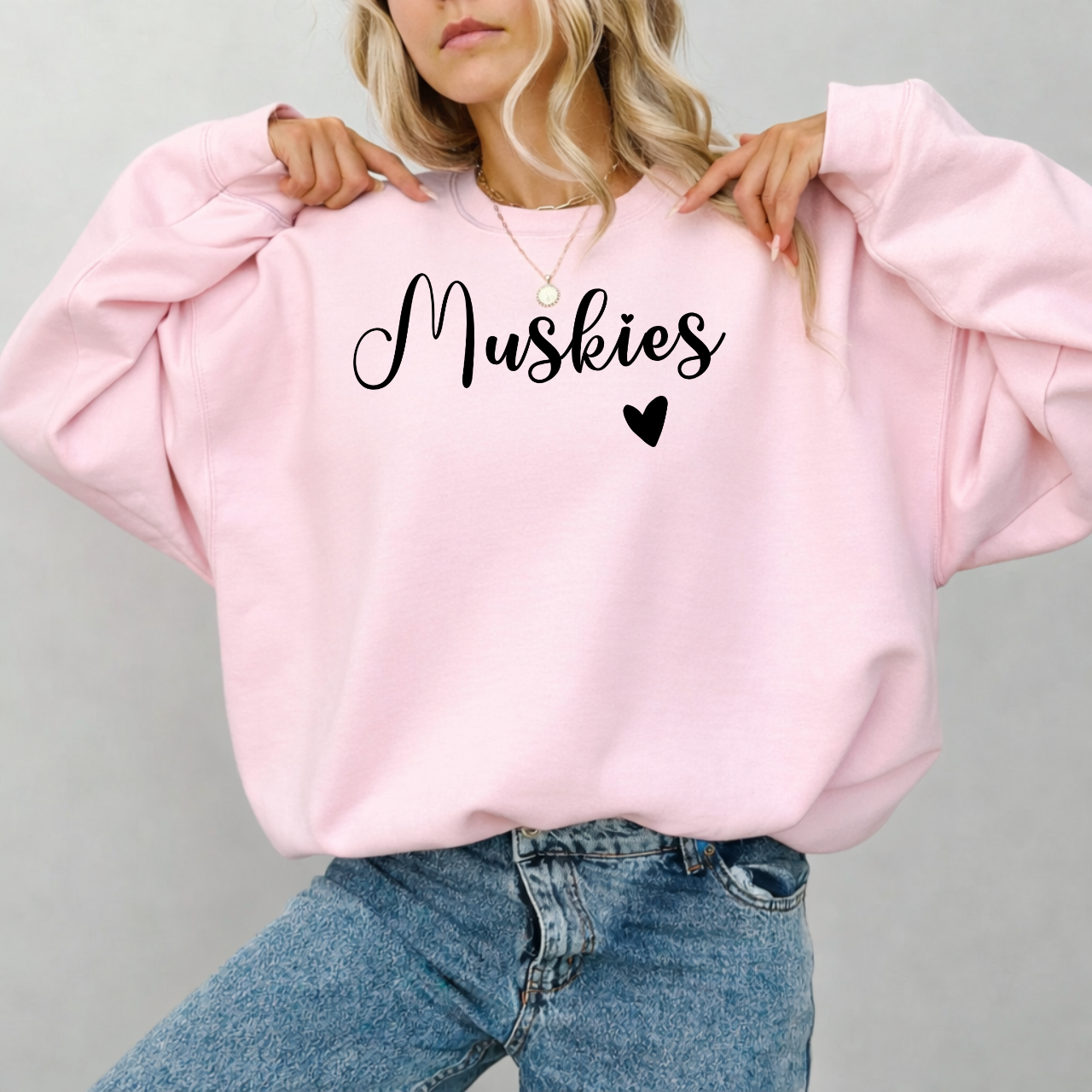 Person wearing a pink sweatshirt with 'Muskies' and a heart design on a gray background