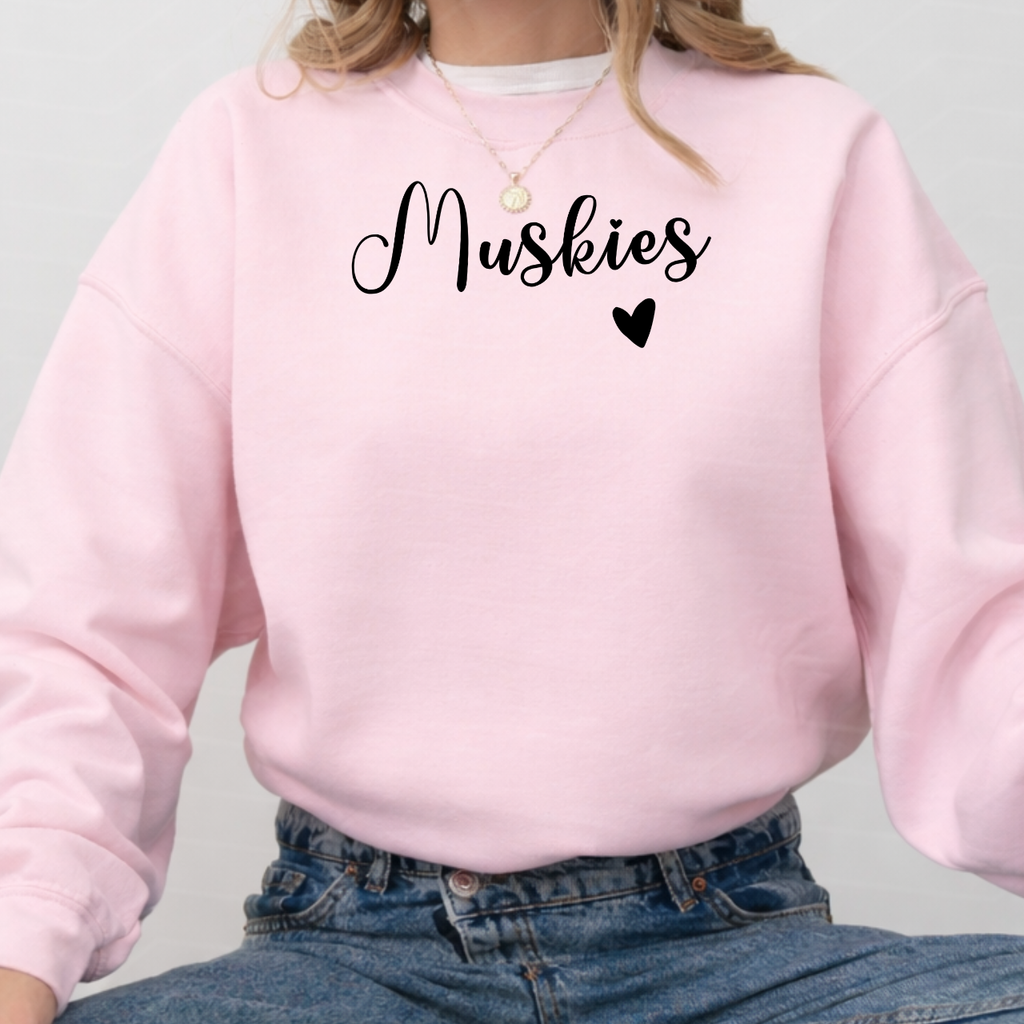 Person wearing a pink sweatshirt with 'Muskies' printed on it against a light gray background