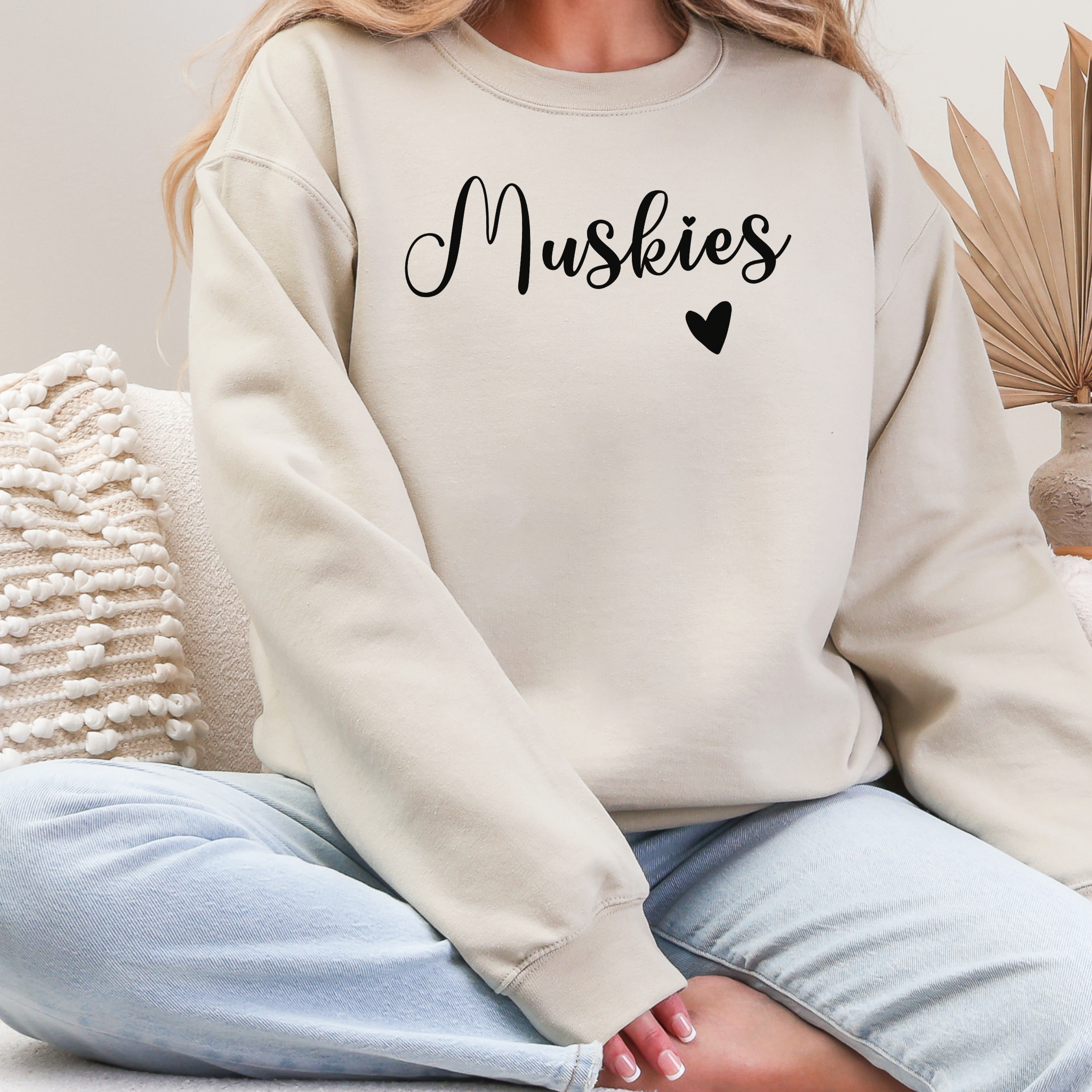 Person wearing a beige sweatshirt with 'Muskies' text and a heart symbol, sitting on a couch.