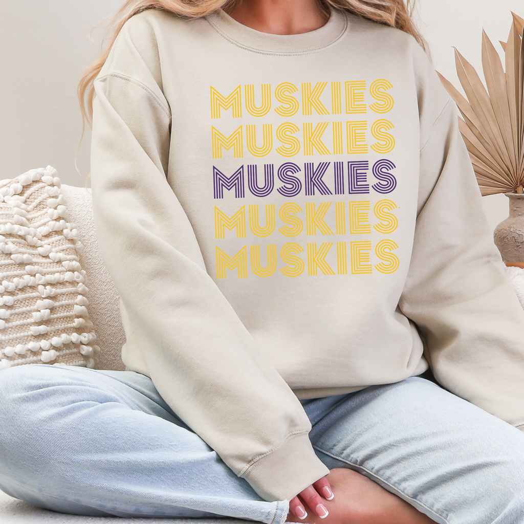 Person wearing a beige sweatshirt with 'Muskies' text in various colors.